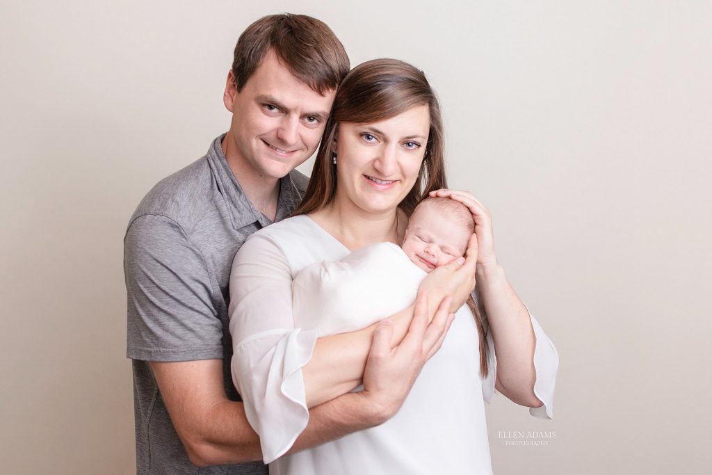 Newborn photographer near me Ellen Adams Photography captured this image of a newborn baby smiling with his family.